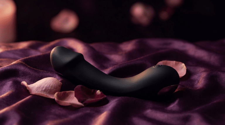 Gode en silicone noir posé sur un drap de soie prune, ambiance boudoir chaleureuse