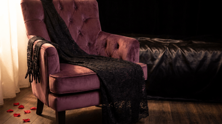 Robe sexy en dentelle noire posée sur un fauteuil de velours prune, ambiance boudoir chaleureuse